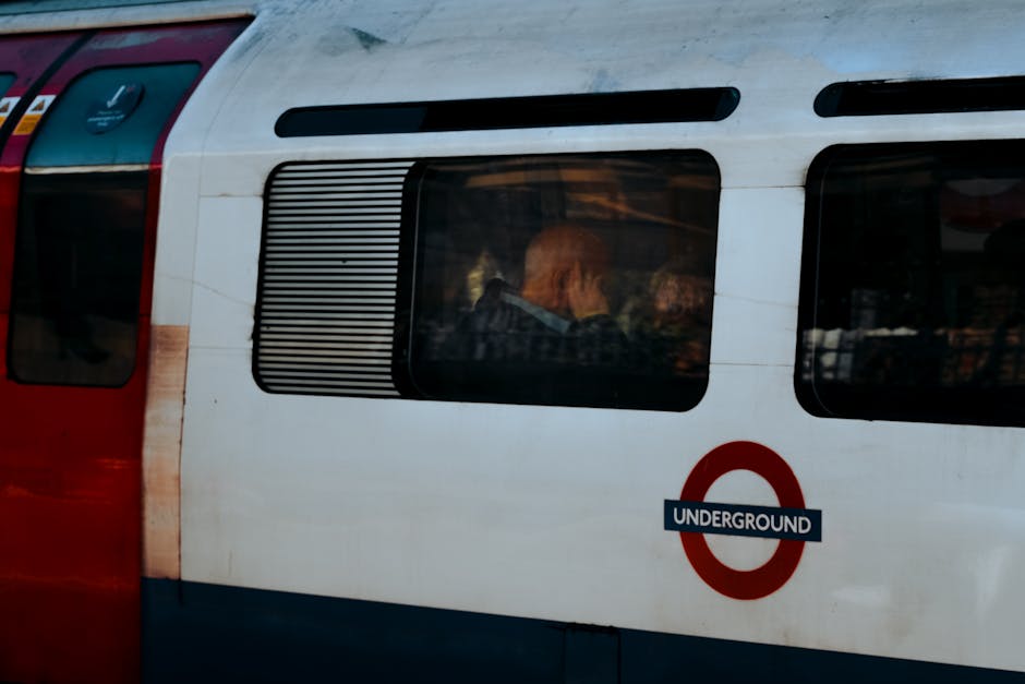Close-up view of a classic outdoor train carriage painted in white and red, featuring a large rectangular window with horizontal black blinds partially covering the glass. Inside the train, visible th